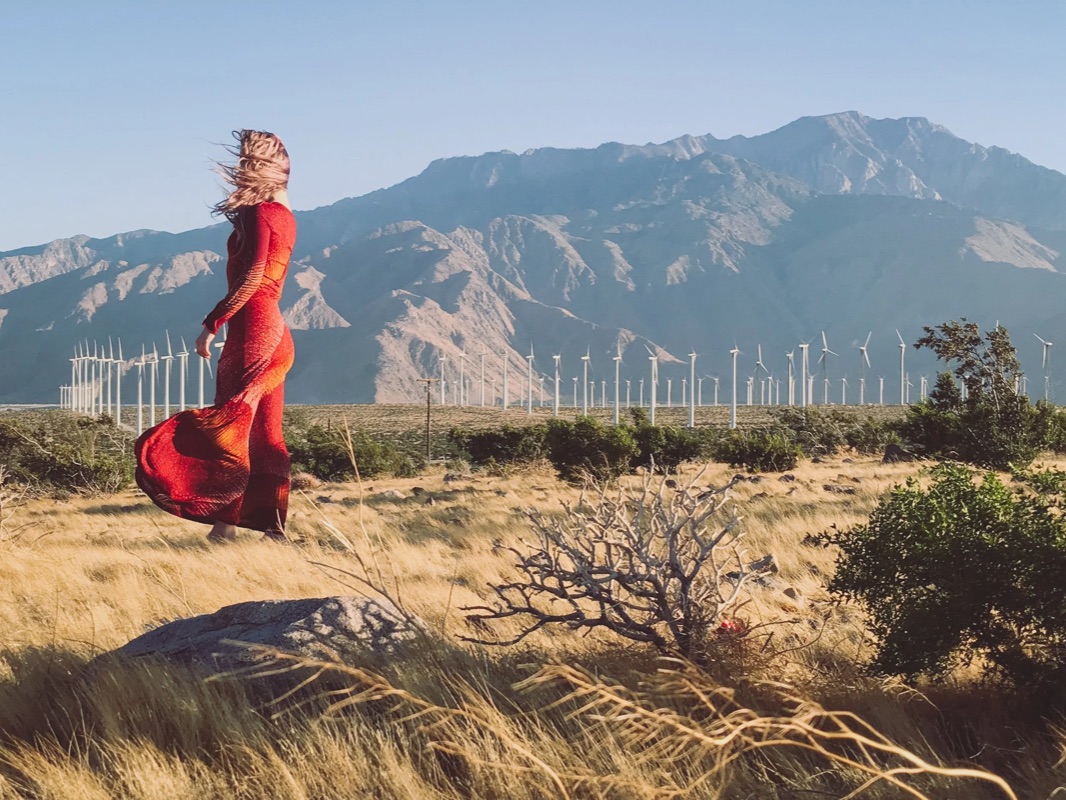 Editorial fashion — woman in a red dress before the Palm Springs windmills and Mount San Jacinto
